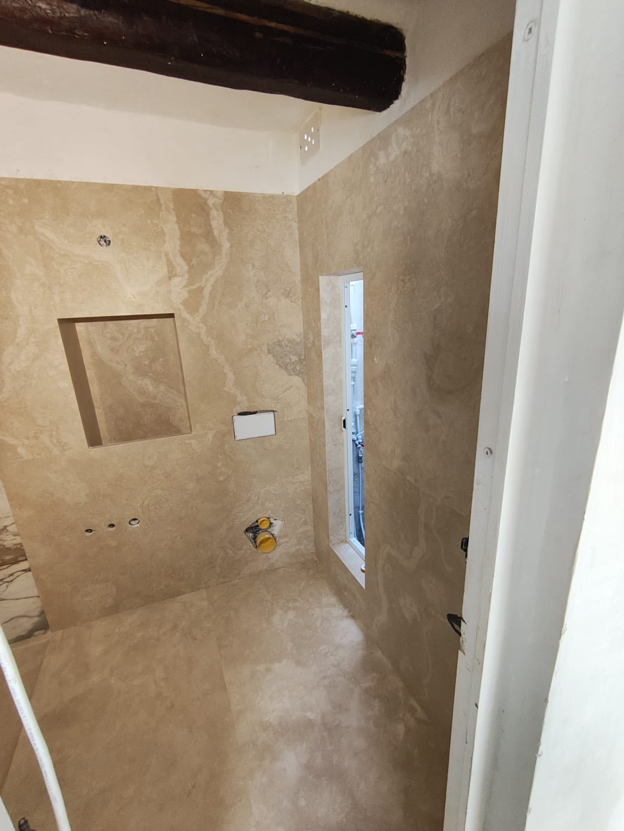A bathroom installation finished with warm natural stone across the walls and floor.