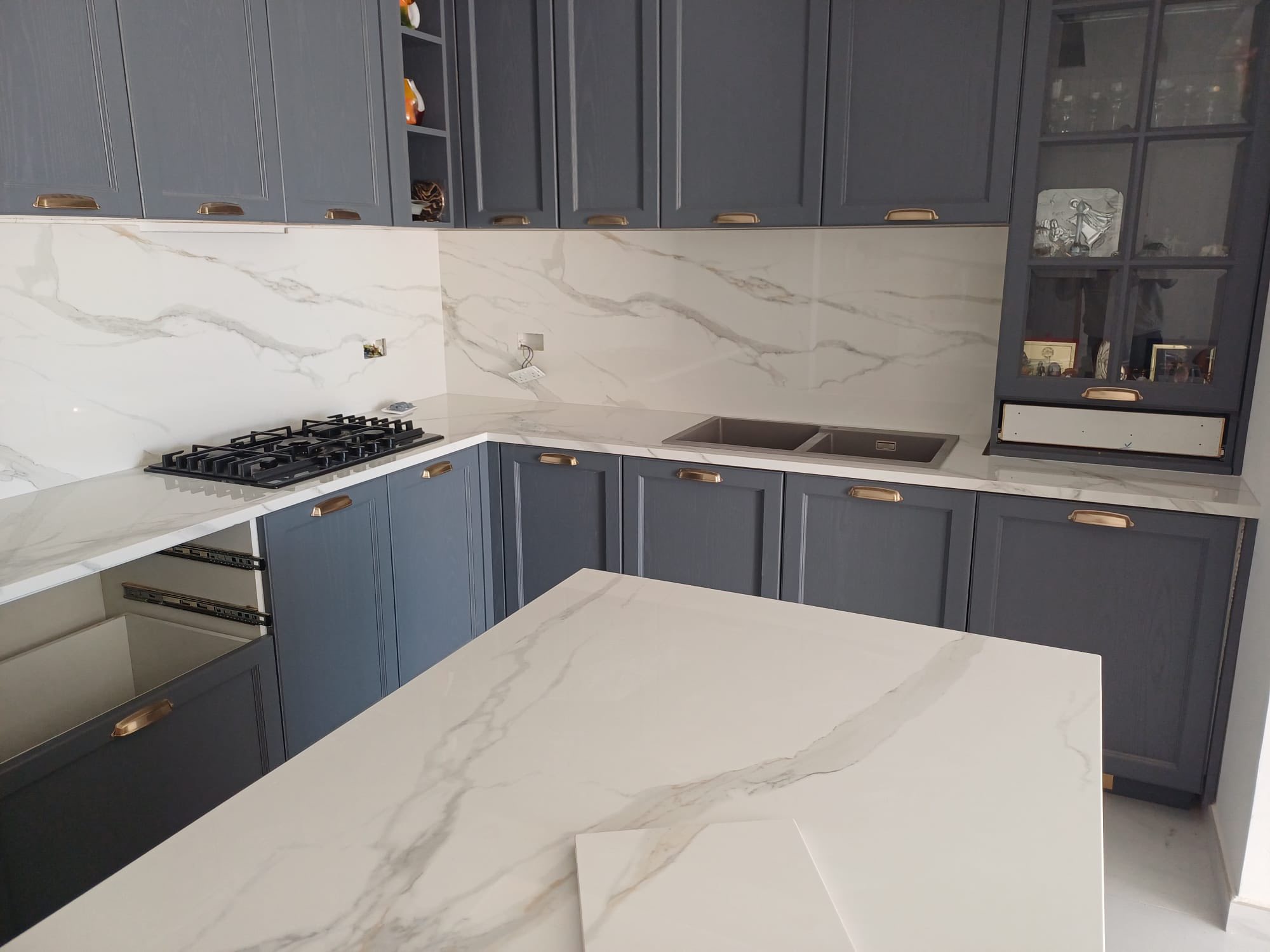 A finished kitchen with marble-look surfaces, blue cabinetry, and a central island.